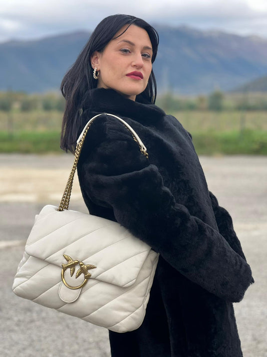 Ragazza che indossa una Borsa Pinko in pelle trapuntata color bianco gesso con parti metalliche dorate; munita di una tracolla in catena scorrevole e spallaccio in pelle. Indossabile a spalla oppure a tracolla. Originale, usata, di lusso, in condizioni buone.