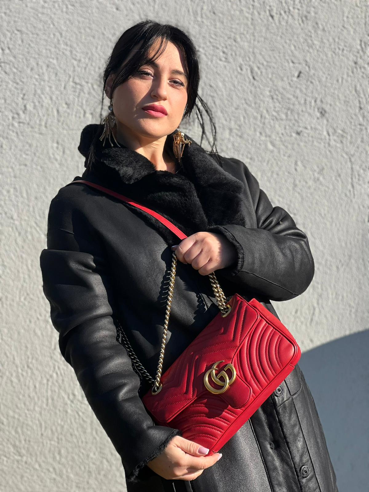 Ragazza che indossa una Borsa Gucci Marmont in pelle matelassé rossa con tracolla scorrevole in catena e spallaccio in pelle, rifinita con parti metalliche dorate. Completa di dustbag. Originale, usato, di lusso, in ottime condizioni.