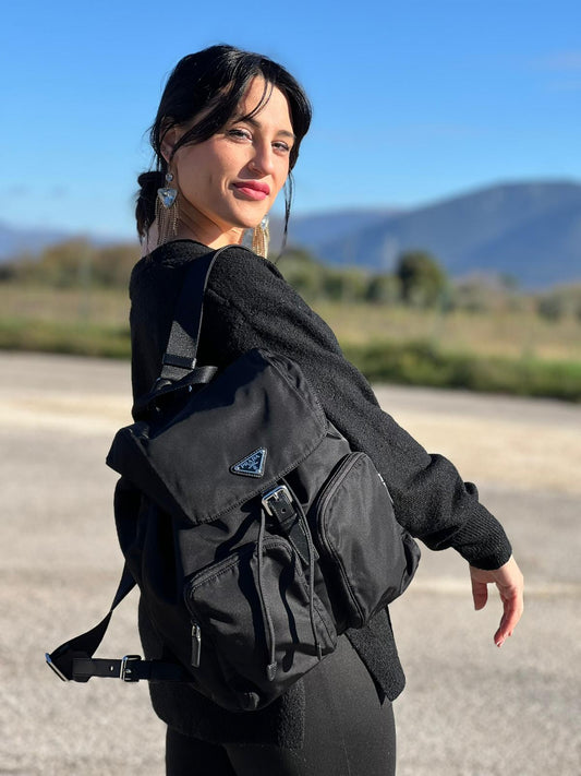 Ragazza che indossa Zaino Prada in tessuto nylon nero e finiture in pelle saffiano tono su tono. Parti metalliche argentate; munito di doppie bretelle in tessuto regolabili. Completo di corredo e card d'autenticità. Originale, usato, di lusso, in condizioni eccellenti.