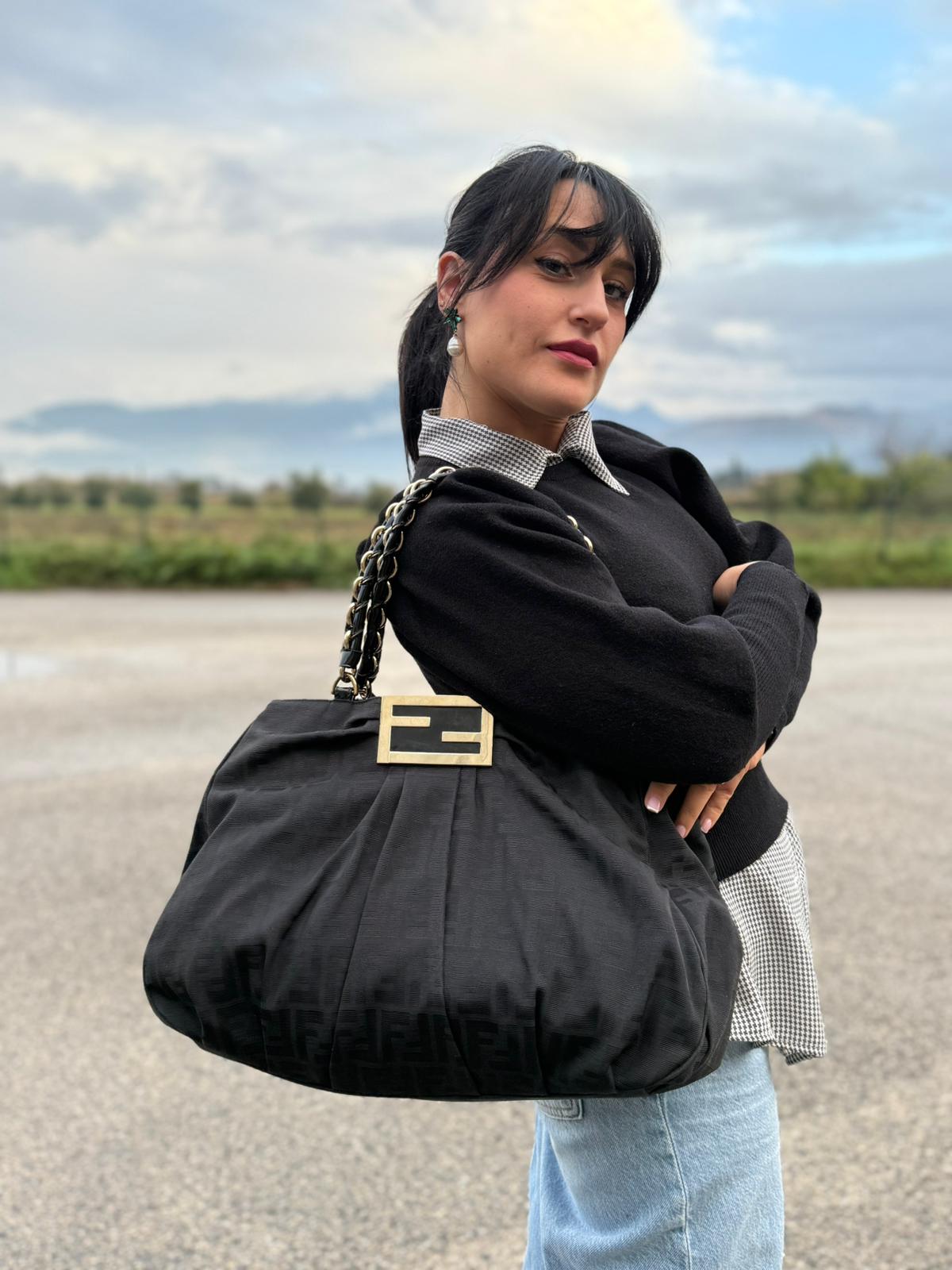 Ragazza che indossa un Borsa Fendi in tessuto nero FF con manici in catena e pelle lucida tono su tono. Parti metalliche dorate. Completa di dustbag. Originale, usata, di lusso, in ottime condizioni.