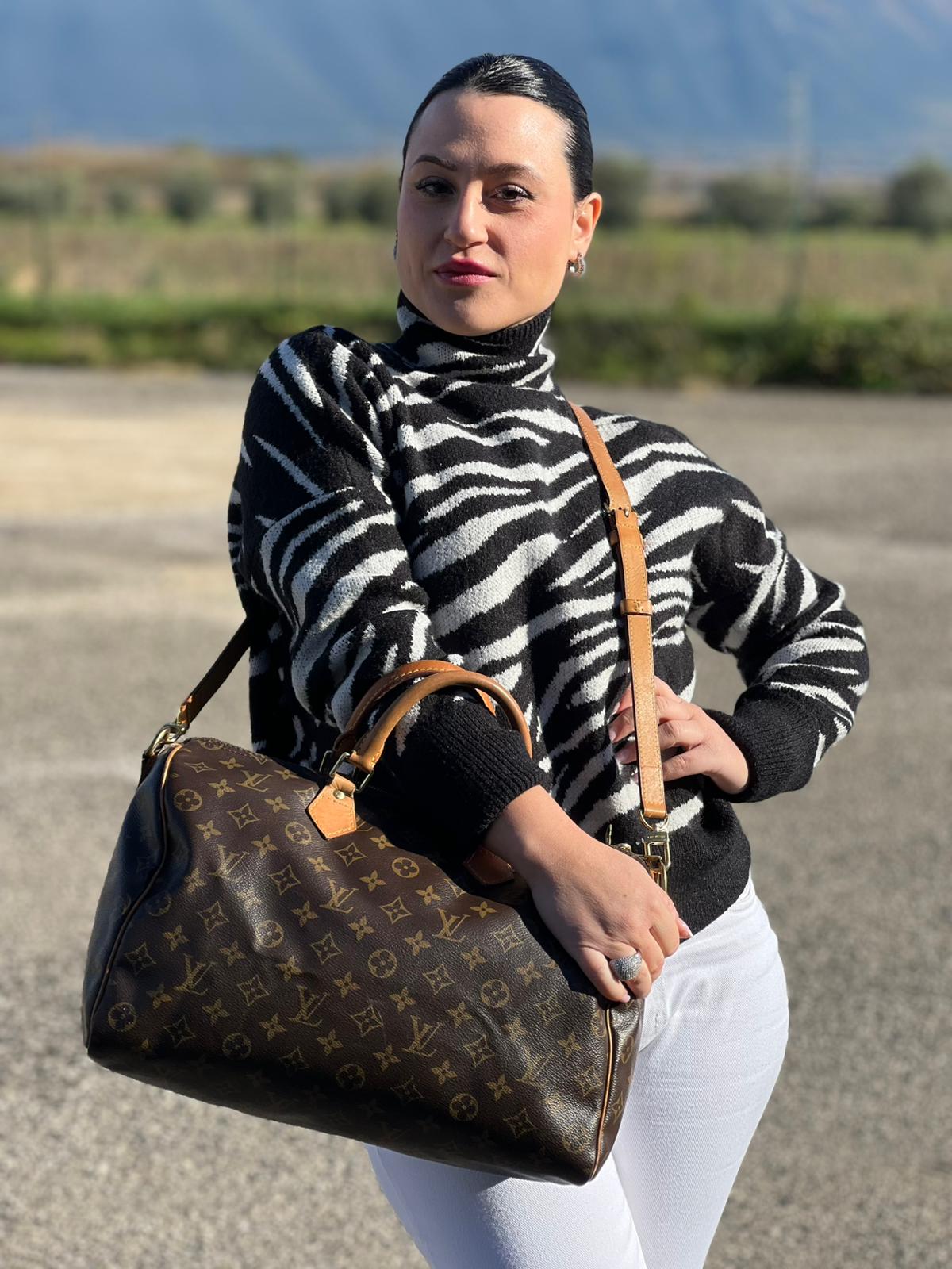 Ragazza che indossa una Borsa Speedy 35 in canvas marrone monogram con finiture in vacchetta naturale e parti metalliche dorate; munita di doppi manici stondati e una tracolla amovibile e regolabile. Completa di lucchetto e chiavi. Originale, usato, di lusso, in ottime condizioni.