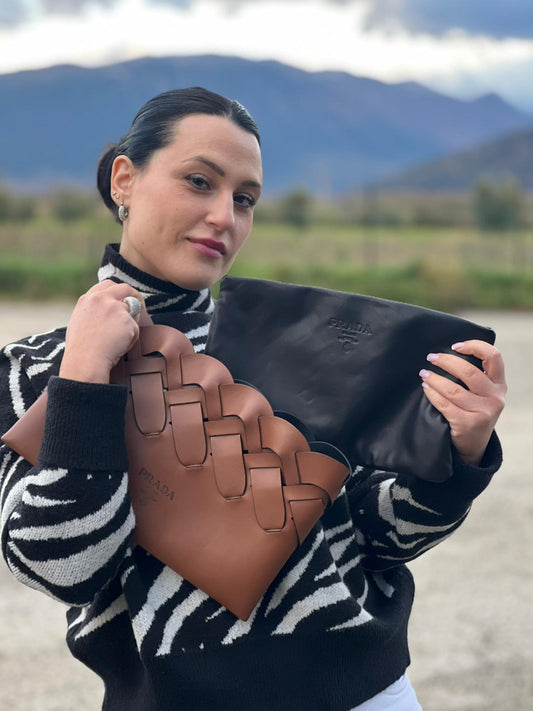 Ragazza che indossa una Pochette Prada in pelle marrone cognac con parti metalliche argentate, presenta un motivo intrecciato nella parte superiore, munita di una pochette estraibile in pelle nera con logo lettering sul front. Originale, usata, di lusso, in ottime condizioni.