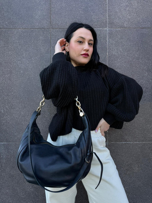 Ragazza che indossa una Borsa Borbonese in pelle nera con parti metalliche dorate. Munita di una tracolla regolabile e un manico in catena con dettagli occhio di pernice non amovibili. Completa di dustbag. Originale, usato, di lusso, in ottime condizioni.