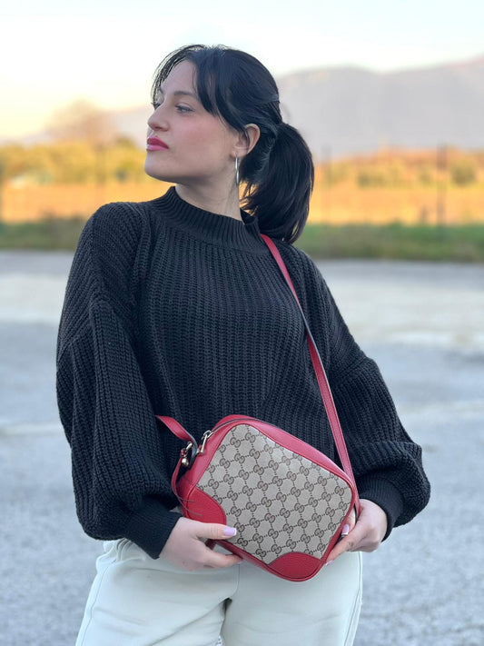 Ragazza che indossa una Borsa Gucci in tessuto GG beige con finiture in pelle martellata rossa e parti metalliche dorate; munita di una tracoll regolabile. Completa di dustbag. Originale, usata, di lusso, in ottime condizioni.
