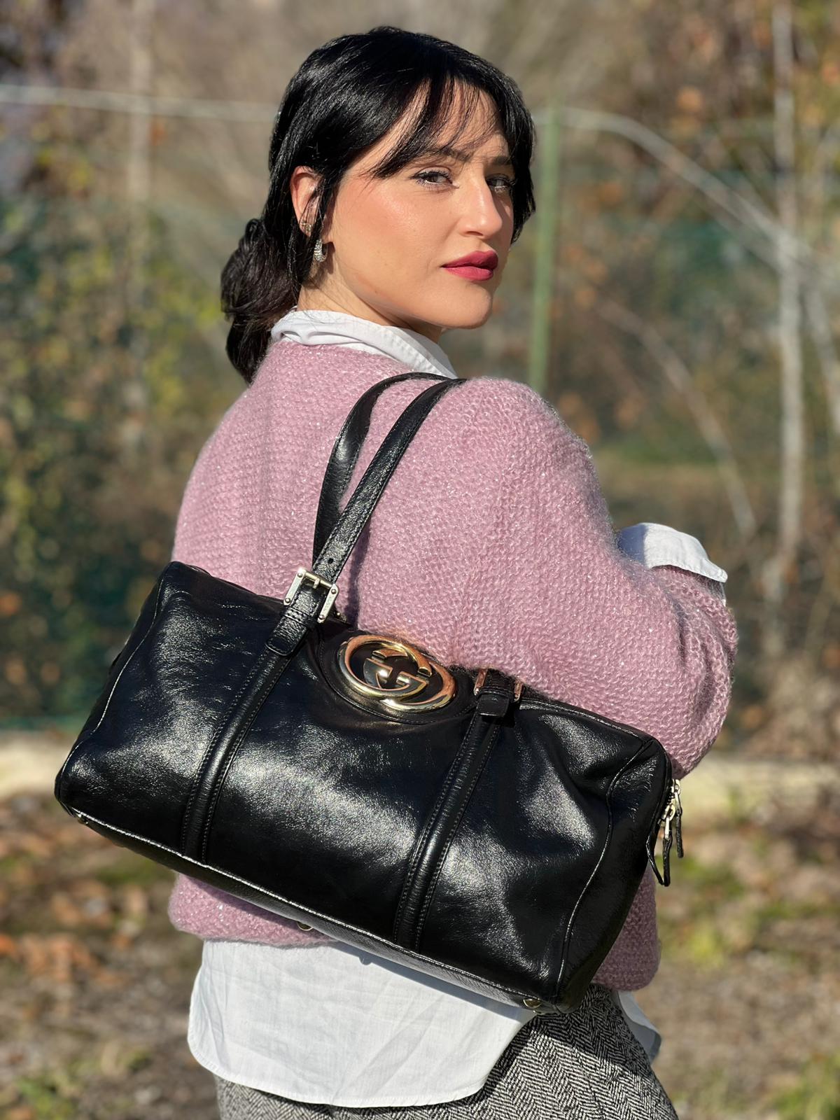 Ragazza che indossa un Bauletto Gucci Britt Boston in pelle nera con parti metalliche dorate e doppi manici; da indossare a spalla. Rifinita con doppie G incrociate in metallo sul front. Completa di dustbag. Originale, usato, di lusso, in ottime condizioni.