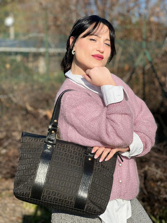 Ragazza che indossa una Borsa Fendi in tessuto nero trama zucchino con parti metalliche dorate, impreziosita li logo fendi lettering su il manico, finiture in pelle nera, munita di due manici. Indossabile a spalla. Originale, usata, di lusso, in ottime condizioni.