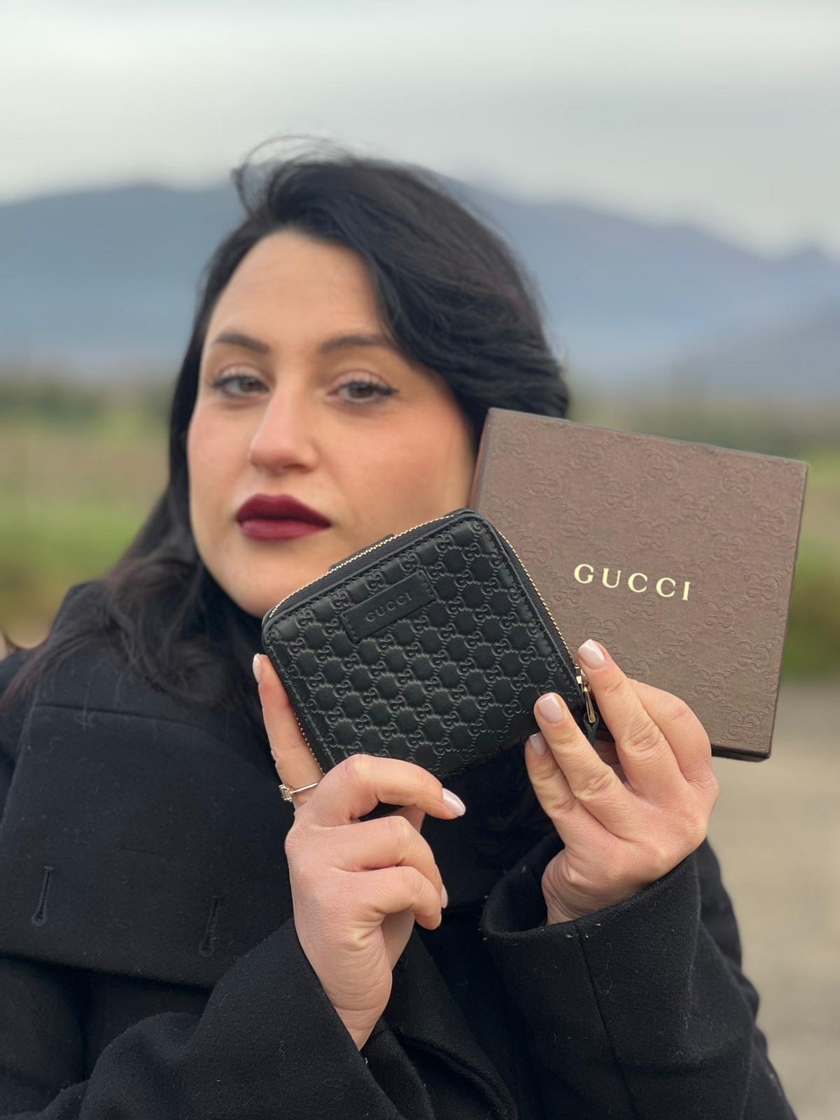 Ragazza che indossa un Portafoglio Gucci in pelle nera GG con parti metalliche dorate. Completo di scatola. Originale, usato, di lusso, in ottime condizioni.