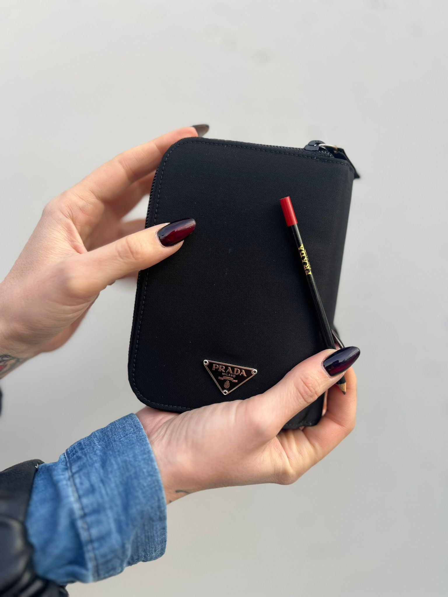 Ragazza che indossa unPorta agenda Prada in tessuto nylon nero e finiture in pelle, con parti metalliche argentate; organizzato con portacarte, portapenne e pratico raccoglitore ad anelli per i fogli. Originale, usato, di lusso, in condizioni eccellenti.