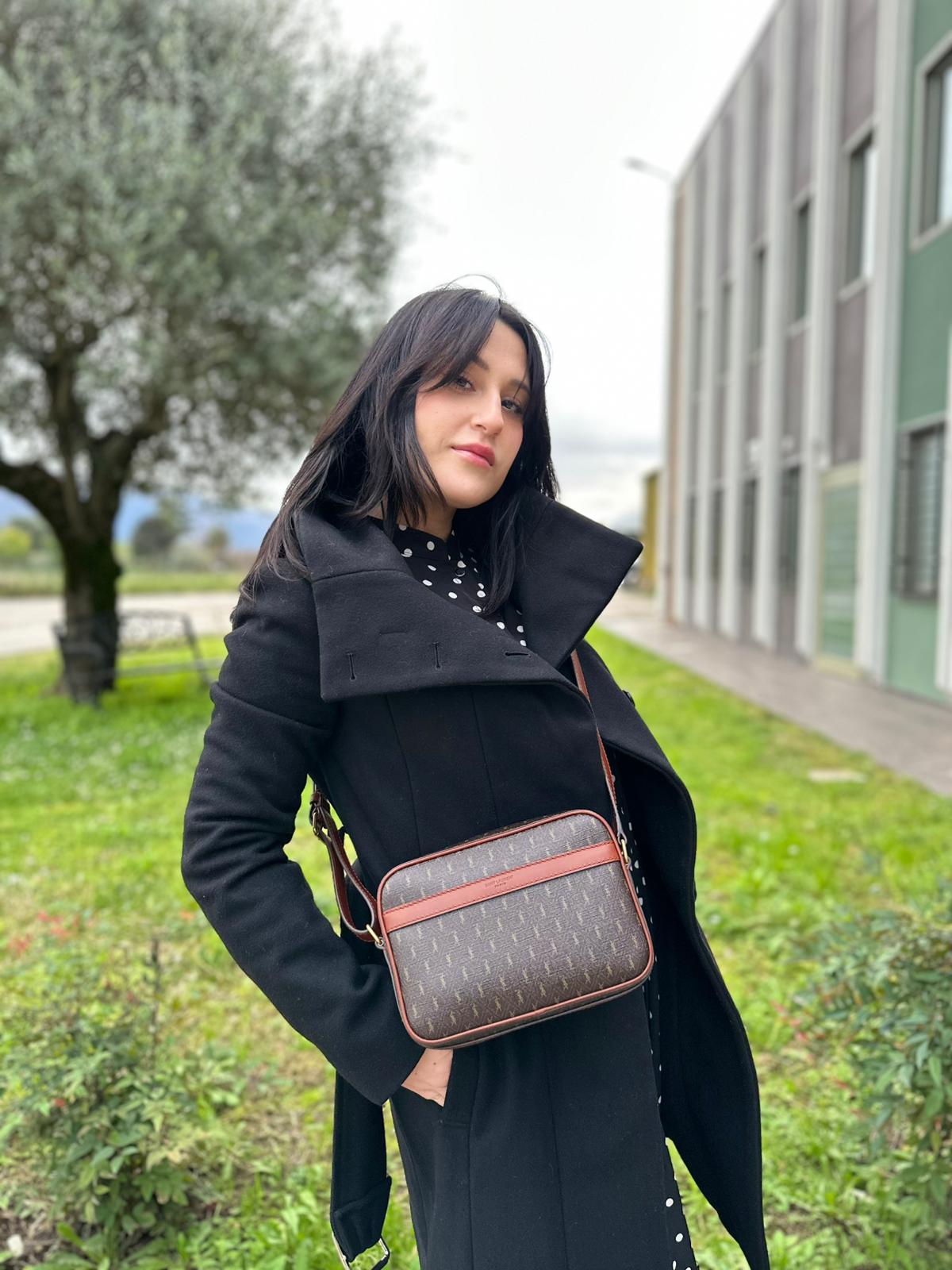 Ragazza che indossa una Borsa Yve Saint Laurent in canvas marrone monogram con parti metalliche dorate e finiture in pelle color cognac; munita di una tracolla leggermente regolabile. Completa di dustbag. Originale, usata, di lusso, in condizioni eccellenti.