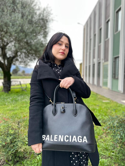Ragazza che indossa una Borsa Balenciaga in pelle martellata nera con parti metalliche dorate, munita di doppi manici e una tracolla amovibile e regolabile. Completa di dustbag e cartellini, lucchetto e chiavi. Originale, usata, di lusso, in ottime condizioni.