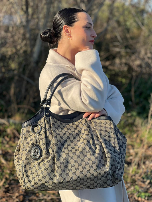 Ragazza che indossa una Borsa Gucci in tessuto beige GG con parti metalliche dorate e parti in pelle color blu notte; munita di doppi manici stondati. Completa di dustbag. Originale, usata, di lusso, in ottime condizioni.