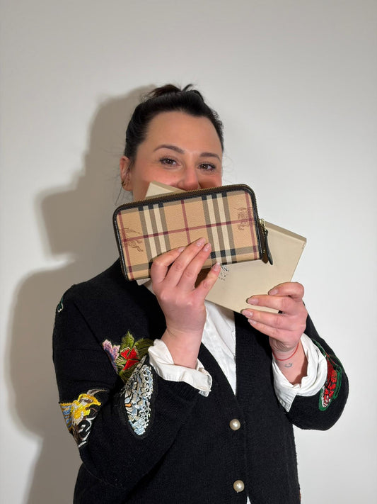 Ragazza che indossa un Portafoglio Burberry in canvas beige trama Burberry check, con interni marroni e parti metalliche dorate. Completo di dustbag e scatola. Originale, usta, di lusso, in ottime condizioni.