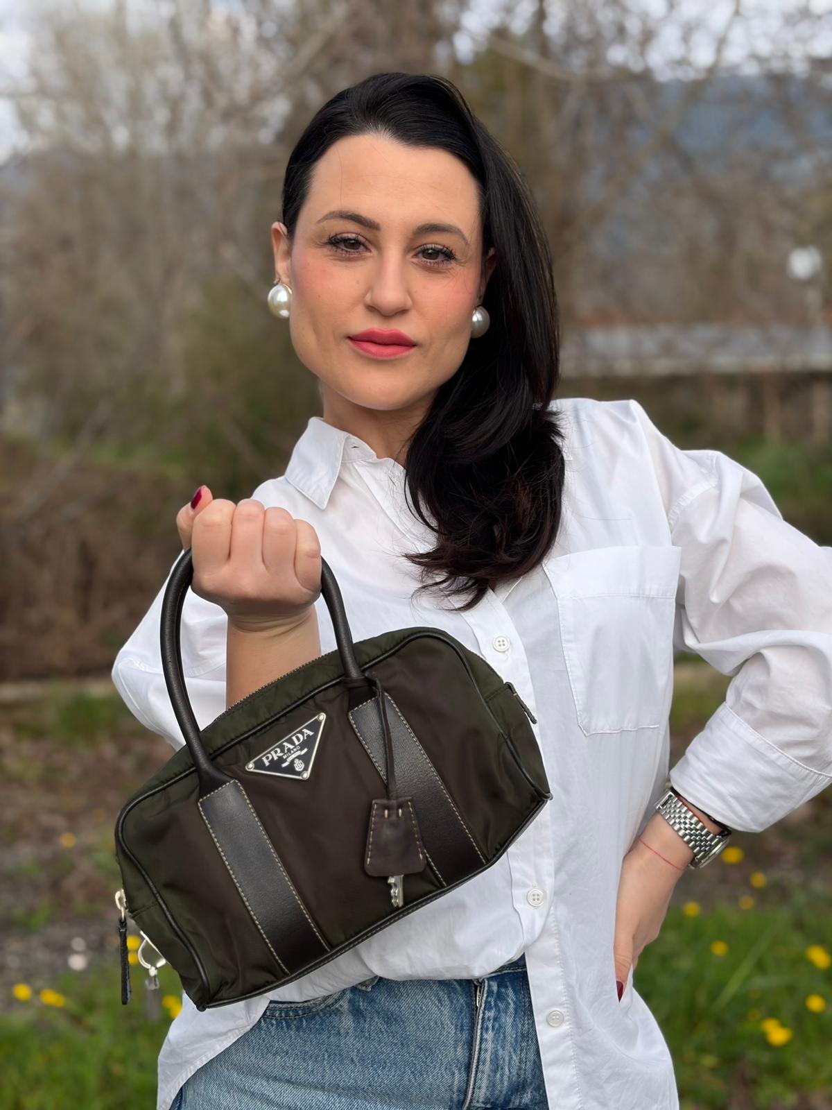 Ragazza che indossa un bauletto Prada in tessuto nylon verde militare e pelle marrone, con dettagli metallici argentati, indossabile a mano.