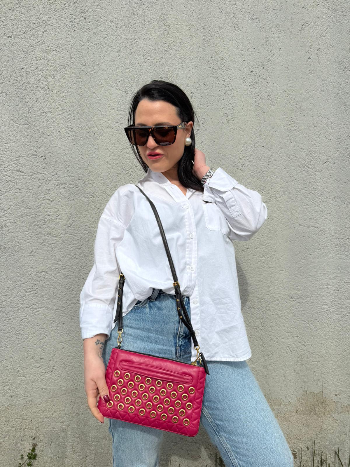 Ragazza che indossa una pochette con tracolla Miu Miu Biker in morbida nappa vele color azalea e hardware dorato, caratterizzata da occhielli metallici, usata, originale, second hand, in ottime condizioni.