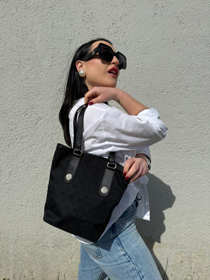 Ragazza che indossa una borsa a spalla Gucci in tessuto nero trama GG, con parti metalliche dorate, usata, originale, second hand, in ottime condizioni.