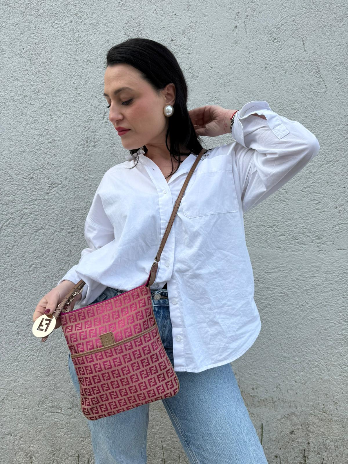 Ragazza che indossa una tracolla Fendi fucsia in trama Zucchino con finiture in pelle color biscotto e piccolo charm logato come tirante, usata, originale, second hand, in ottime condizioni.