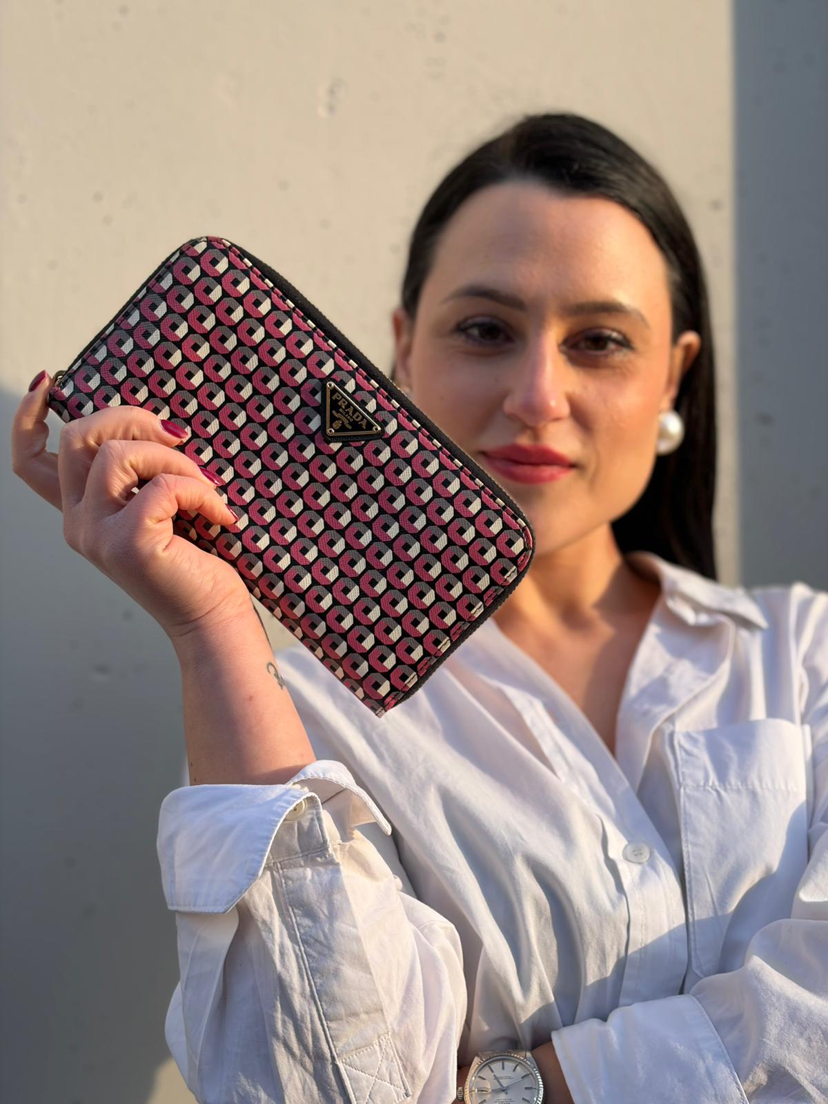 Ragazza che mostra un portafoglio Prada in pelle saffiano multicolore, decorato con stampa geometrica, usato, originale, second hand, in ottime condizioni.