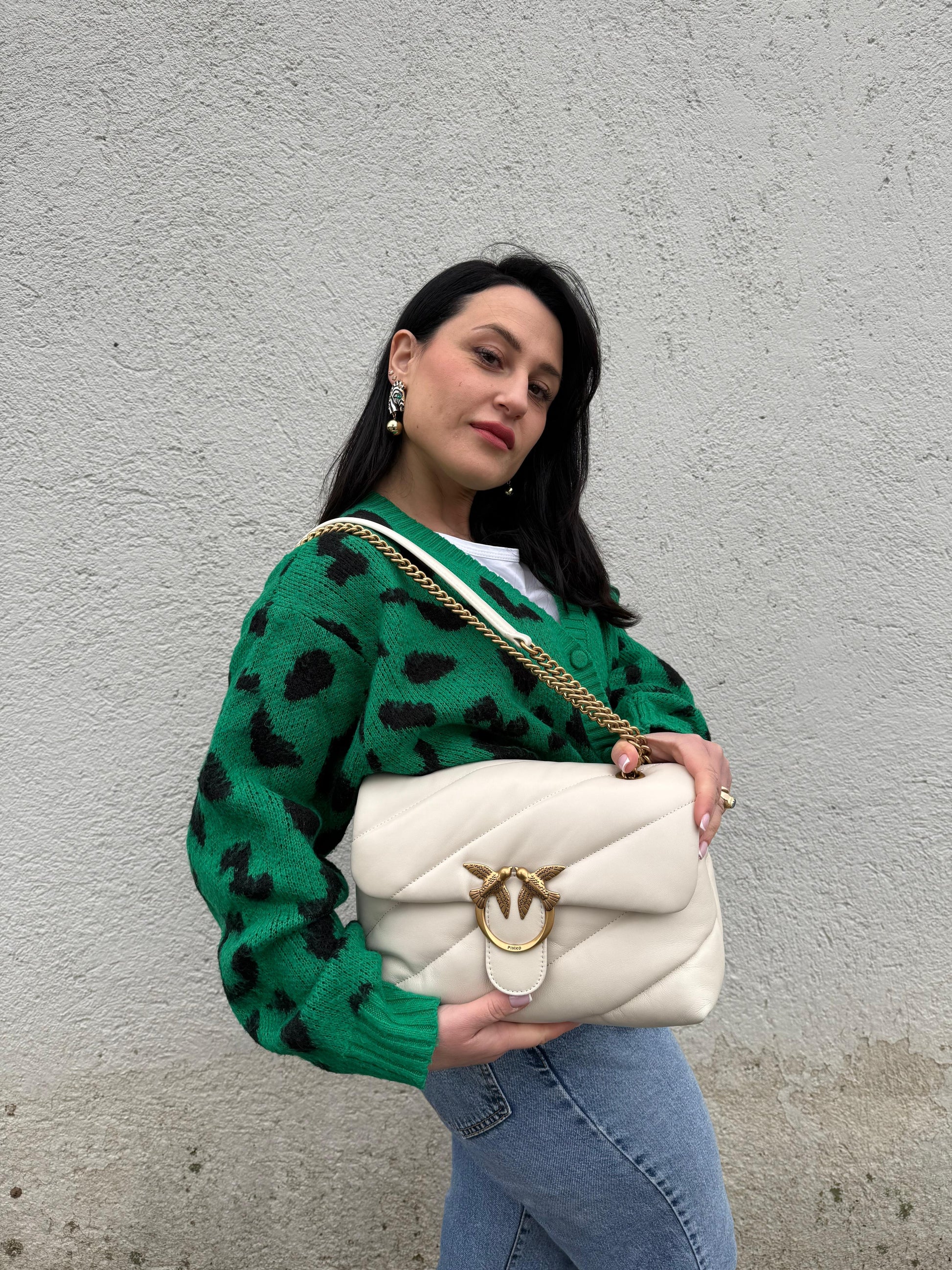 Ragazza che indossa una borsa Pinko in pelle trapuntata bianco latte con parti metalliche dorate; munita di una tracolla in catena scorrevole con spallaccio in pelle. Completa di dustbag e cartellino. Indossabile a spalla o a tracolla.