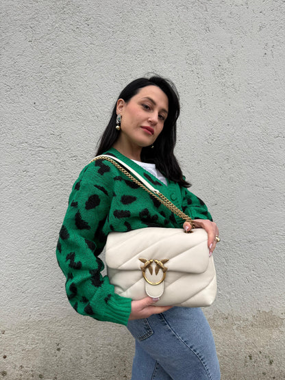 Ragazza che indossa una borsa Pinko in pelle trapuntata bianco latte con parti metalliche dorate; munita di una tracolla in catena scorrevole con spallaccio in pelle. Completa di dustbag e cartellino. Indossabile a spalla o a tracolla.