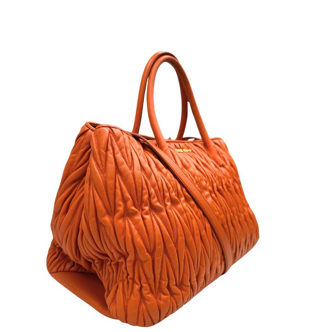 Lato destro di una  Borsa Miu Miu realizzata in nappa matelassé arancione con parti metalliche dorate; munita di due manici stondati e una tracolla regolabile amovibile. Originale, usata, di lusso, in ottime condizioni