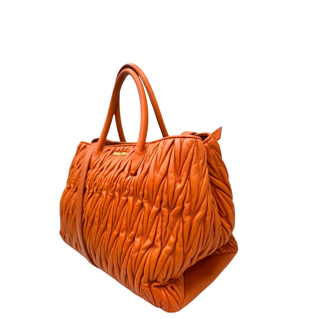 Lato sinistro di una Borsa Miu Miu realizzata in nappa matelassé arancione con parti metalliche dorate; munita di due manici stondati e una tracolla regolabile amovibile. Originale, usata, di lusso, in ottime condizioni