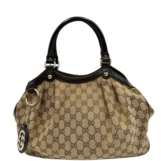 Front di una Borsa Gucci Sukey in tessuto beige GG con finiture in pelle color marrone testa di moro, doppi manici arrotondati e ciondolo con doppie G incrociate. Rifinita con parti metalliche dorate. Originale, usata, di lusso, in ottime condizioni.