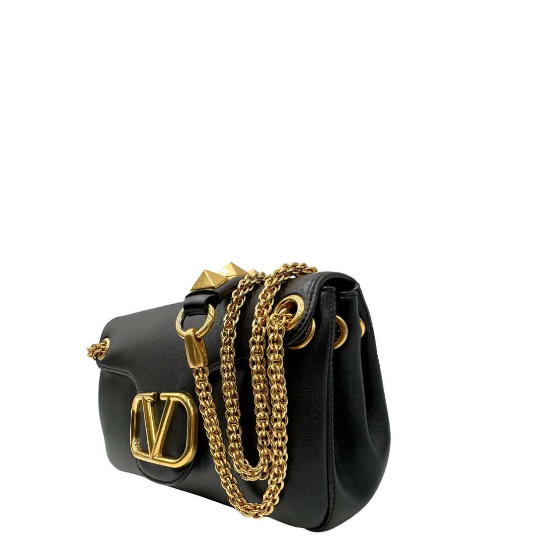 Lato sinistro di una Borsa Stud Sign Valentino Garavani in pelle nera con parti metalliche dorate e tracolla in catena scorrevole con borchie piramidali dorate sullo spallaccio. Completa di dustbag e cartellino. Originale, usata, di lusso, in ottime condizioni