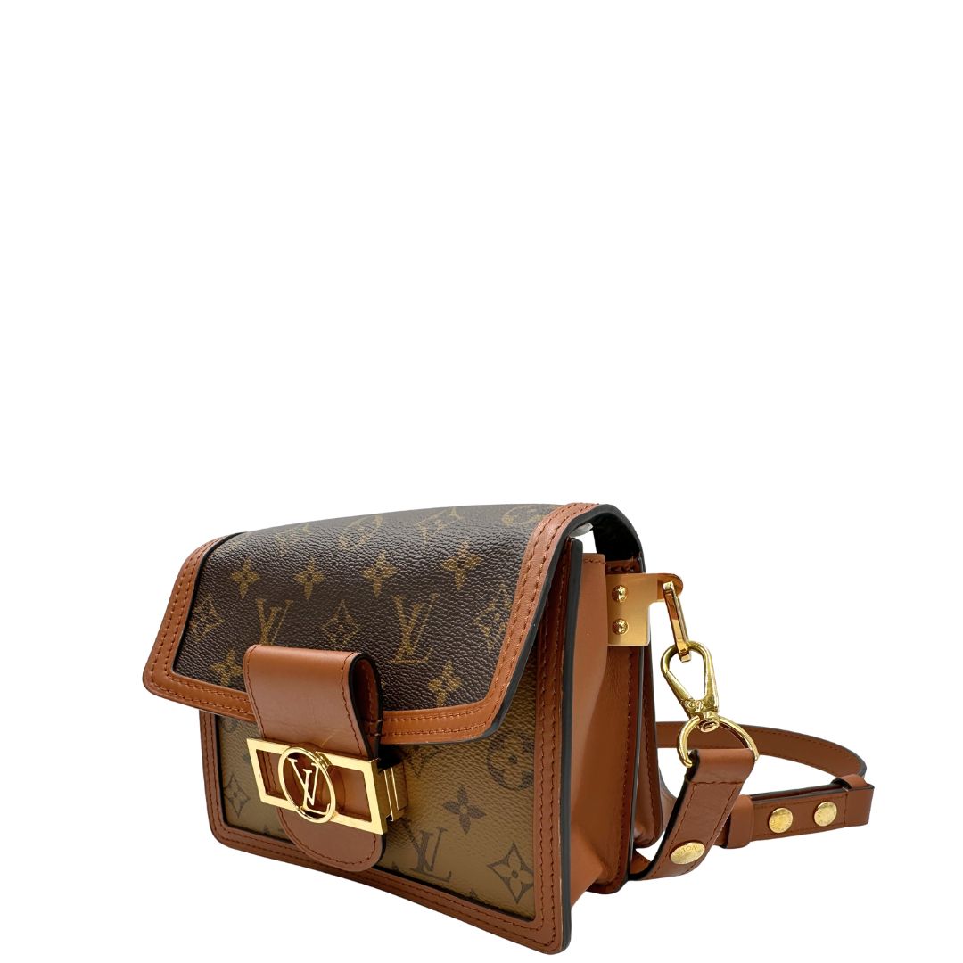 Lato sinistro di una Borsa Dauphine Mini Louis Vuitton in tela monogram, e monogram reverse bicolore con finiture in pelle cognac e parti metalliche dorate, munita di una tracolla in pelle allungabile e un manico in catena, amovibili. Originale, usata, di lusso, in ottime condizioni