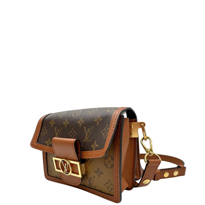 Lato sinistro di una Borsa Dauphine Mini Louis Vuitton in tela monogram, e monogram reverse bicolore con finiture in pelle cognac e parti metalliche dorate, munita di una tracolla in pelle allungabile e un manico in catena, amovibili. Originale, usata, di lusso, in ottime condizioni