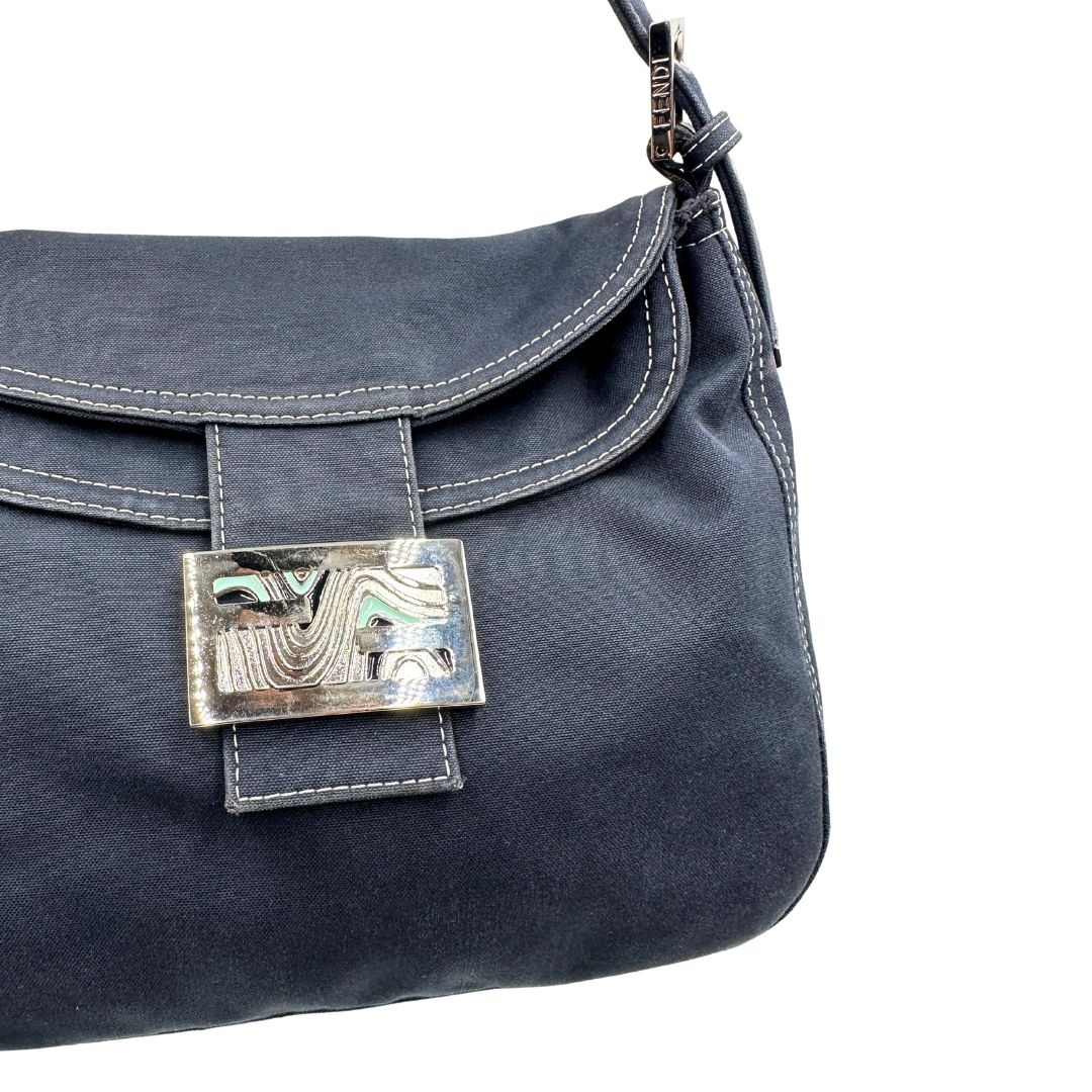 Chiusura di una borsa Fendi realizzata in tessuto blu navy con cuciture bianche a contrasto, manico leggermente regolabile e con parti metalliche argentate. Iconico logo effetto marble sulla chiusura della patta. Indossabile a spalla.