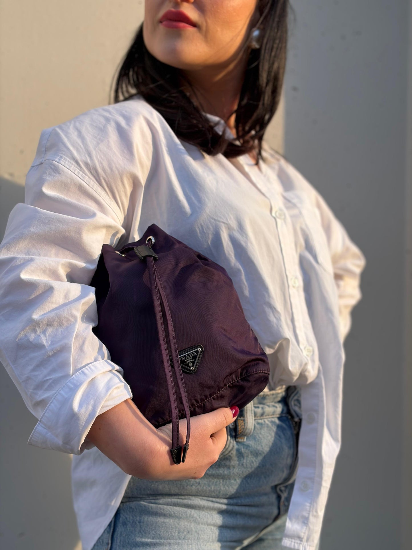 Ragazza che indossa una pochette Prada in tessuto nylon viola e hardware argentato, usata, originale, second hand, in ottime condizioni.