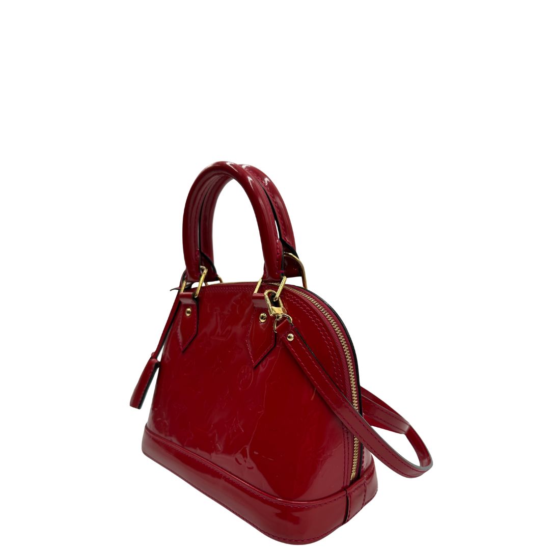 lato Borsa Louis Vuitton Alma BB in pelle vernis rossa con trama monogram empreinte e parti metalliche dorate. Munita di doppi manici stondati e tracolla amovibile, dotata di clochette porta chiavi. Completa di scatola, lucchetto e chiavi, di lusso, originale, ottime condizioni. 