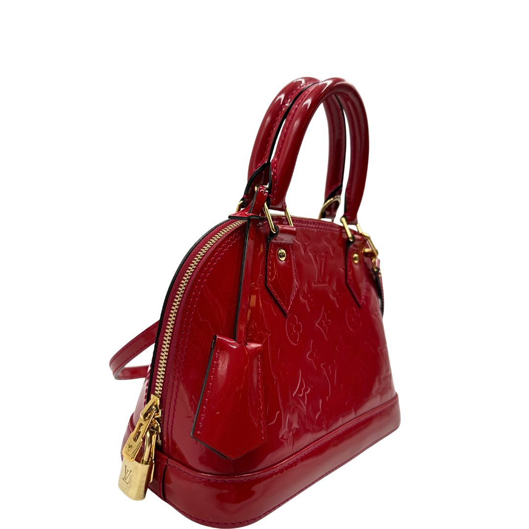 lato Borsa Louis Vuitton Alma BB in pelle vernis rossa con trama monogram empreinte e parti metalliche dorate. Munita di doppi manici stondati e tracolla amovibile, dotata di clochette porta chiavi. Completa di scatola, lucchetto e chiavi, di lusso, originale, ottime condizioni. 