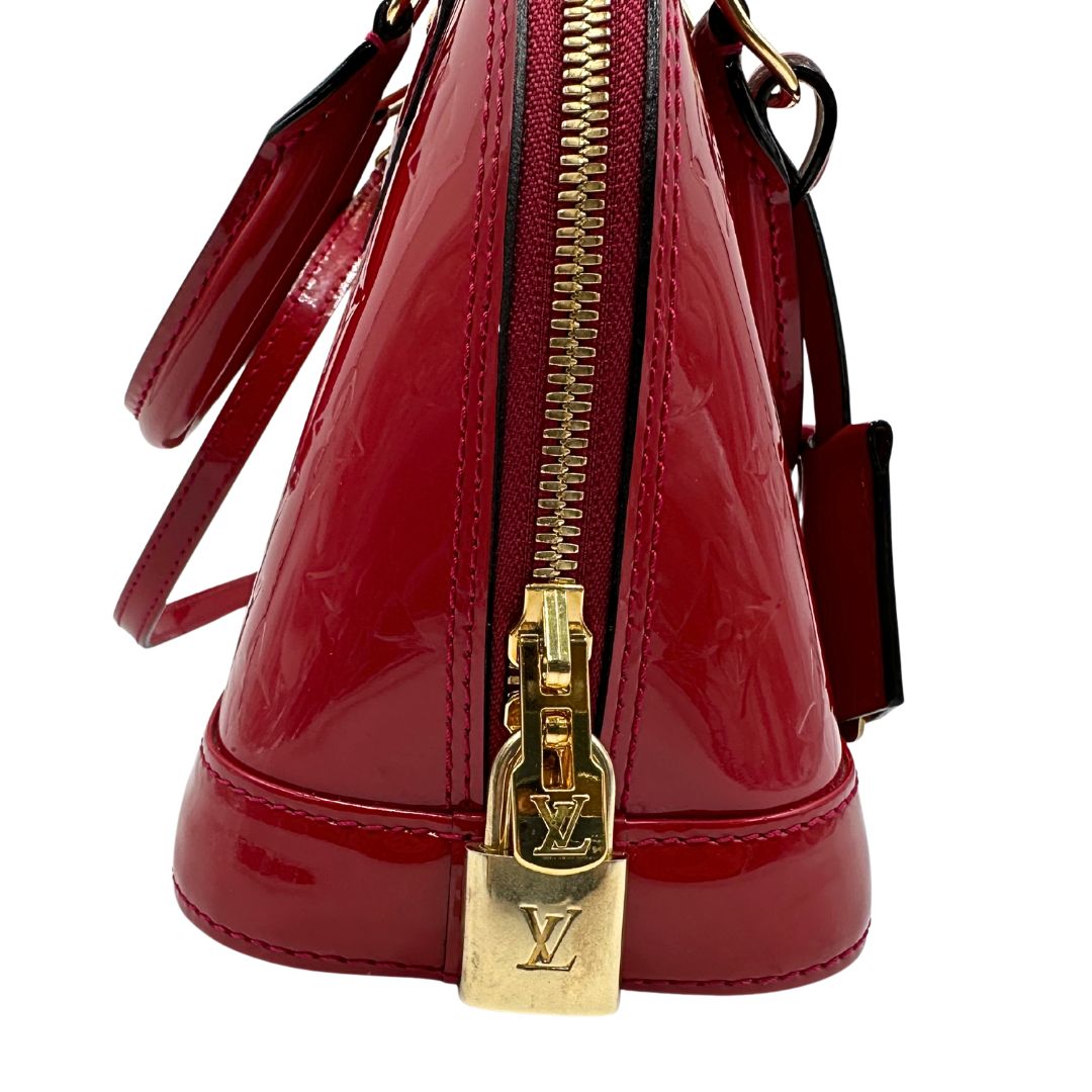 lucchetto Borsa Louis Vuitton Alma BB in pelle vernis rossa con trama monogram empreinte e parti metalliche dorate. Munita di doppi manici stondati e tracolla amovibile, dotata di clochette porta chiavi. Completa di scatola, lucchetto e chiavi, di lusso, originale, ottime condizioni. 