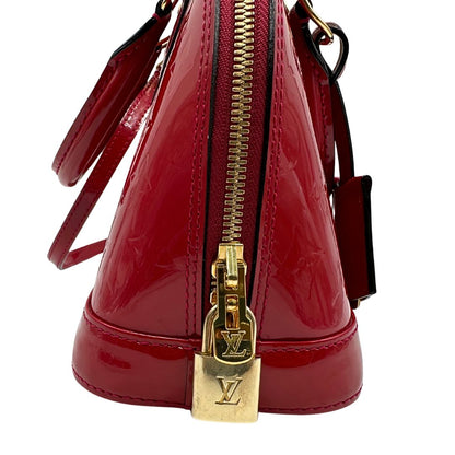 lucchetto Borsa Louis Vuitton Alma BB in pelle vernis rossa con trama monogram empreinte e parti metalliche dorate. Munita di doppi manici stondati e tracolla amovibile, dotata di clochette porta chiavi. Completa di scatola, lucchetto e chiavi, di lusso, originale, ottime condizioni. 