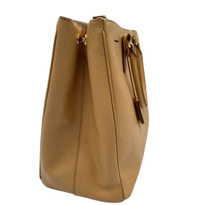 lato  Borsa Prada in pelle saffiano color nocciola con parti metalliche dorate; munita di doppi manici stondati e impreziosita da una clochette portachiavi. Completa di dustbag, di lusso, originale, buone condizioni. 