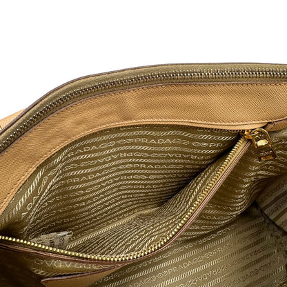 interno  Borsa Prada in pelle saffiano color nocciola con parti metalliche dorate; munita di doppi manici stondati e impreziosita da una clochette portachiavi. Completa di dustbag, di lusso, originale, buone condizioni. 
