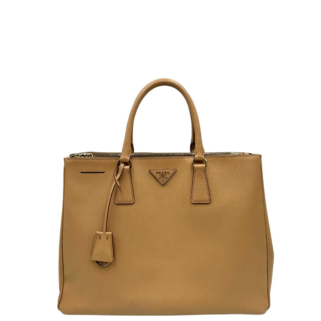 front  Borsa Prada in pelle saffiano color nocciola con parti metalliche dorate; munita di doppi manici stondati e impreziosita da una clochette portachiavi. Completa di dustbag, di lusso, originale, buone condizioni. 