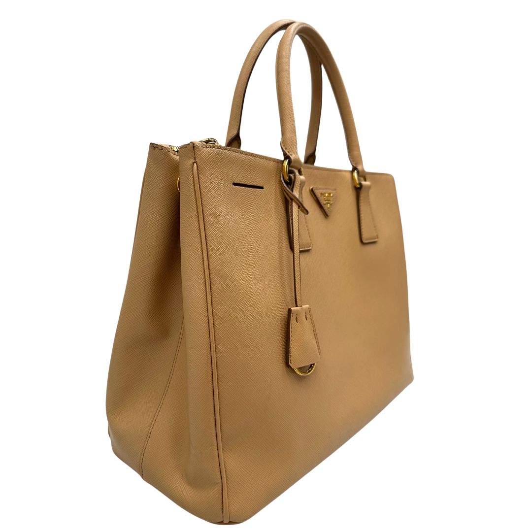 lato  Borsa Prada in pelle saffiano color nocciola con parti metalliche dorate; munita di doppi manici stondati e impreziosita da una clochette portachiavi. Completa di dustbag, di lusso, originale, buone condizioni. 