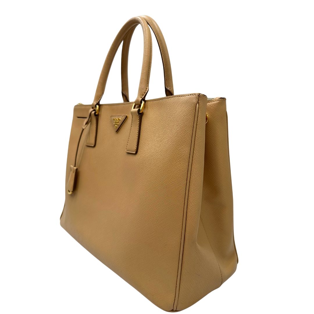 lato  Borsa Prada in pelle saffiano color nocciola con parti metalliche dorate; munita di doppi manici stondati e impreziosita da una clochette portachiavi. Completa di dustbag, di lusso, originale, buone condizioni. 