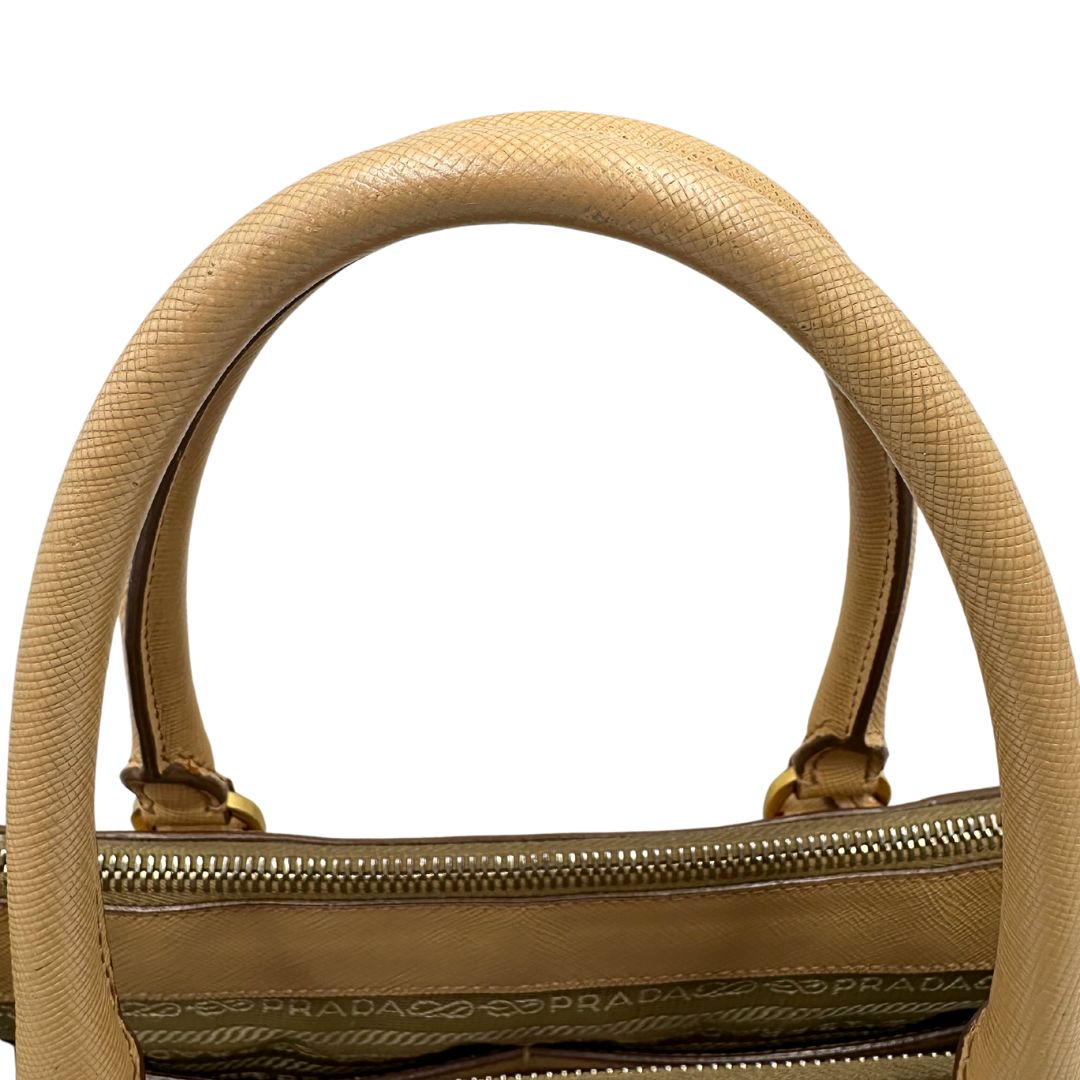 manici  Borsa Prada in pelle saffiano color nocciola con parti metalliche dorate; munita di doppi manici stondati e impreziosita da una clochette portachiavi. Completa di dustbag, di lusso, originale, buone condizioni. 