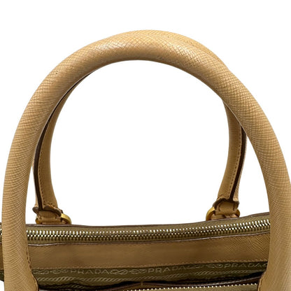 manici  Borsa Prada in pelle saffiano color nocciola con parti metalliche dorate; munita di doppi manici stondati e impreziosita da una clochette portachiavi. Completa di dustbag, di lusso, originale, buone condizioni. 