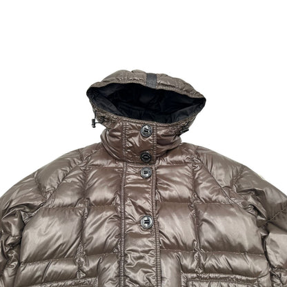Piumino Moncler in tessuto lucido color marrone, con parti metalliche effetto renio, in 100% poliammide, caratterizzato da imbottitura trapuntata, chiusura con zip e bottoni logati, cappuccio regolabile e polsini interni a coste per una maggiore protezione dal freddo.