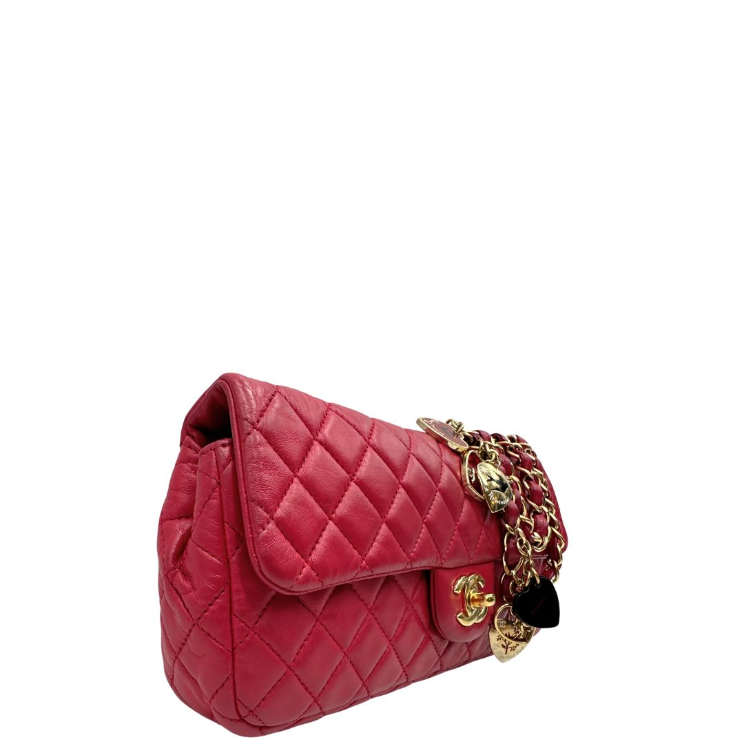 Lato destro di una Borsa Chanel Gabrielle in pelle matelassé color fucsia con parti metalliche dorate; impreziosita da charm con cuoricini sulla tracolla intrecciata in catena e pelle. Completa di scatola e card di autenticità. Originale, usata, di lusso in ottime condizioni