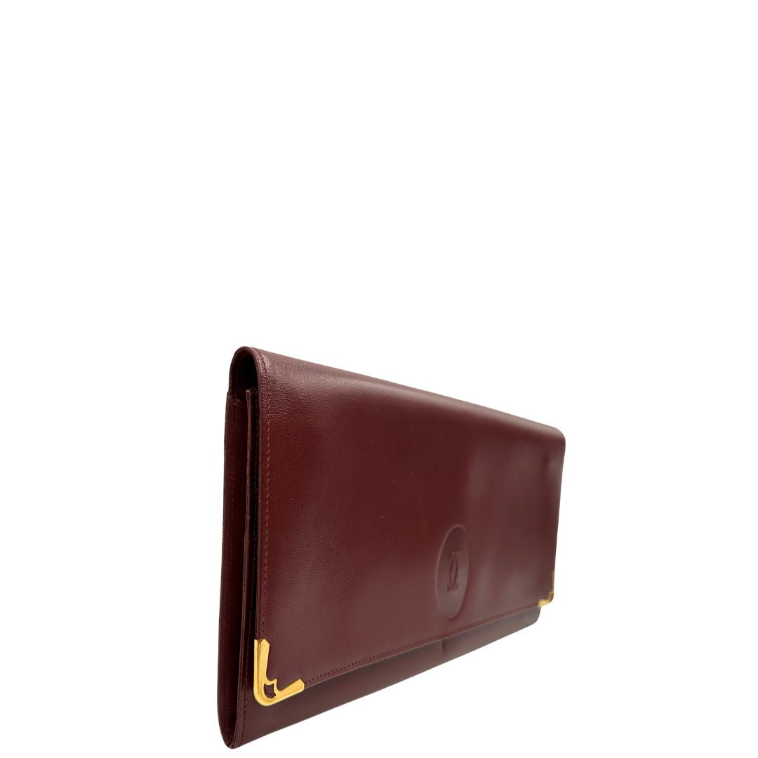 lato  Clutch Les Must de Cartier in pelle bordeaux con parti metalliche dorate. Munito di scatola, di lusso, originale. 