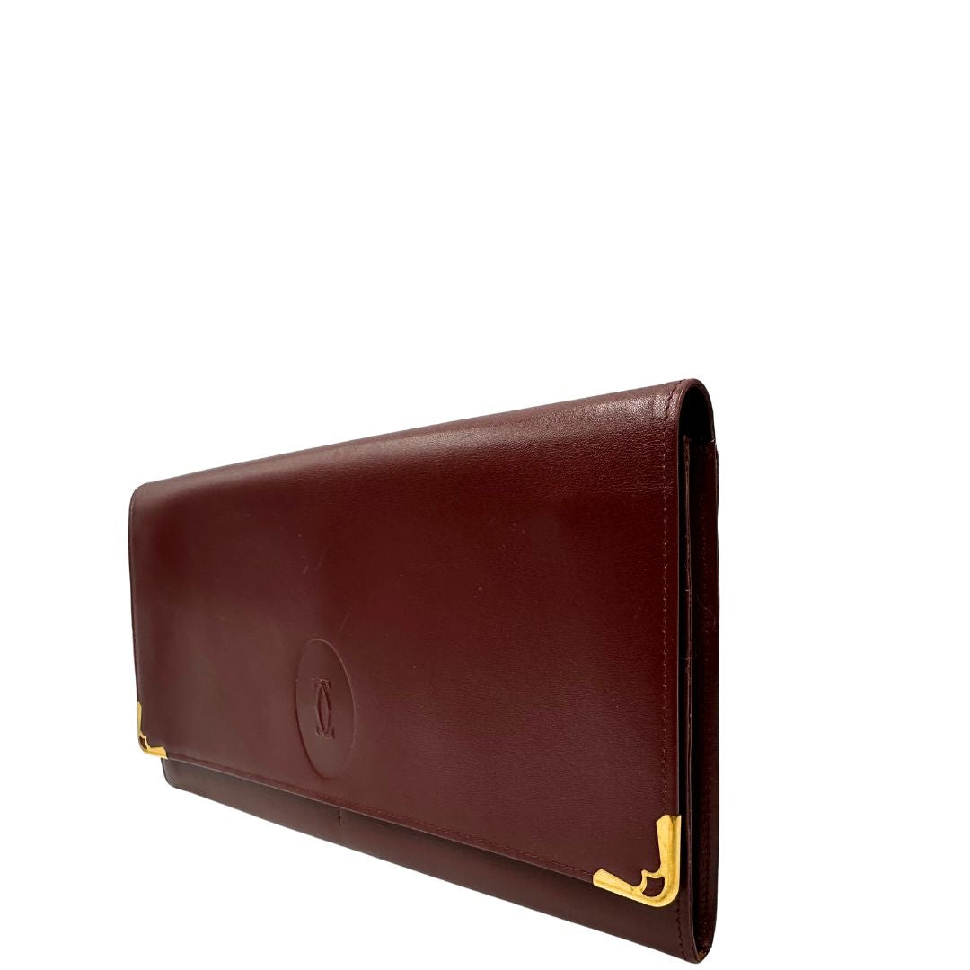 lato Clutch Les Must de Cartier in pelle bordeaux con parti metalliche dorate. Munito di scatola, di lusso, originale.