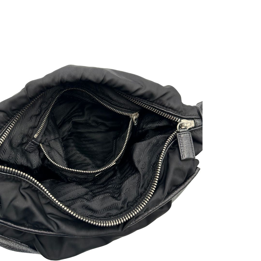 Interno di una Borsa Prada in nylon nero con parti metalliche argentate e dettagli in pelle tono su tono. Munita di una tracolla regolabile con fibbie, rifinita con logo triangolare sul lato destro. Originale, usata, di lusso, in condizioni buone.