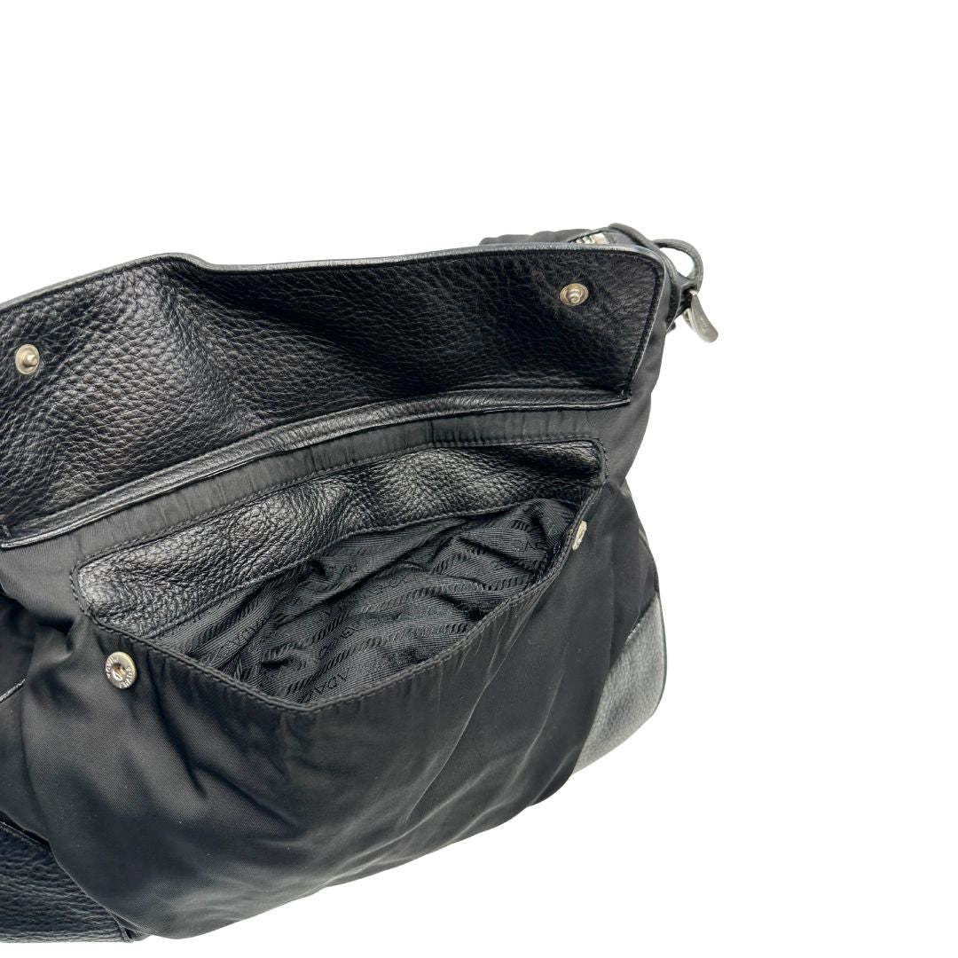 Tasca esterna di una Borsa Prada in nylon nero con parti metalliche argentate e dettagli in pelle tono su tono. Munita di una tracolla regolabile con fibbie, rifinita con logo triangolare sul lato destro. Originale, usata, di lusso, in condizioni buone.
