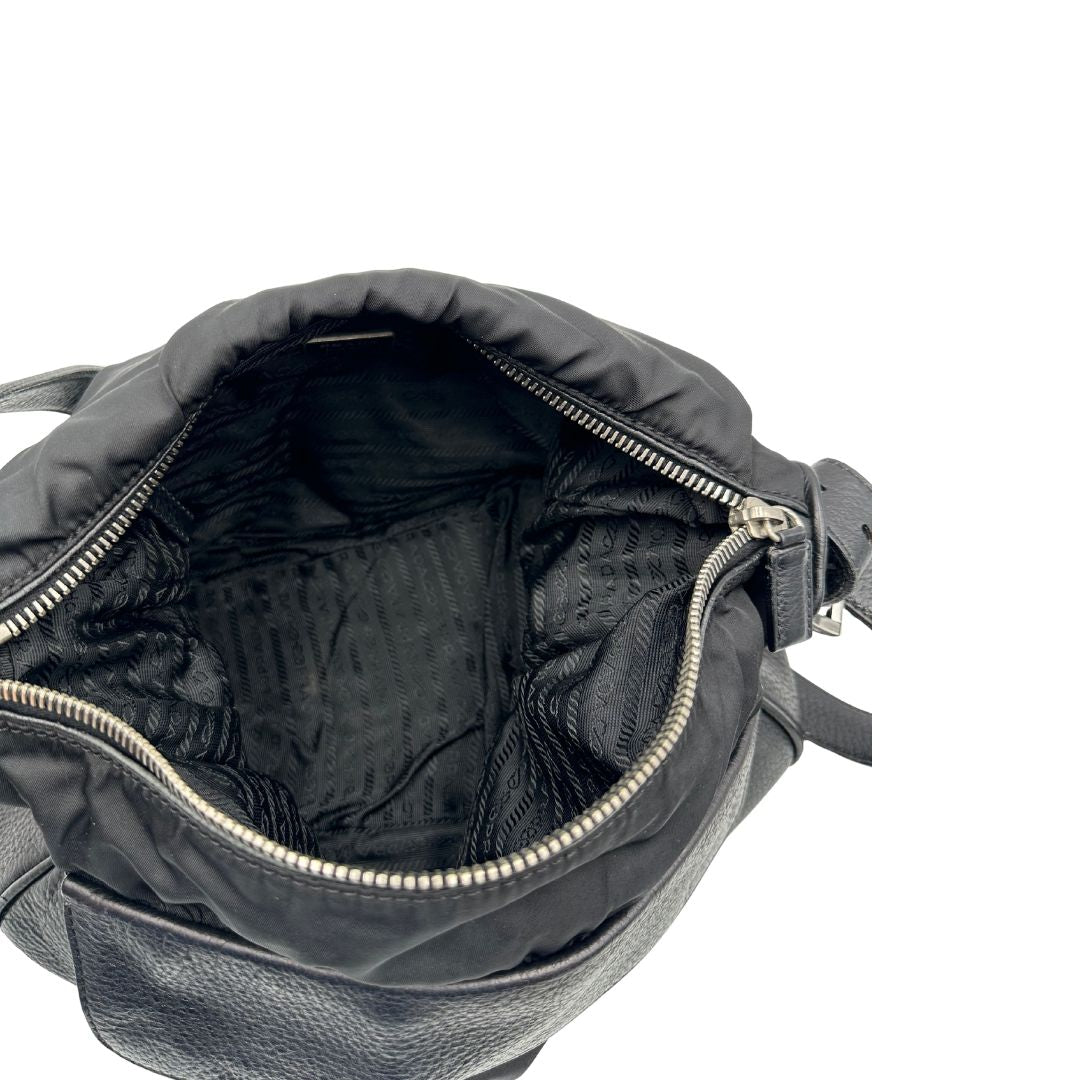 Interno di una Borsa Prada in nylon nero con parti metalliche argentate e dettagli in pelle tono su tono. Munita di una tracolla regolabile con fibbie, rifinita con logo triangolare sul lato destro. Originale, usata, di lusso, in condizioni buone.