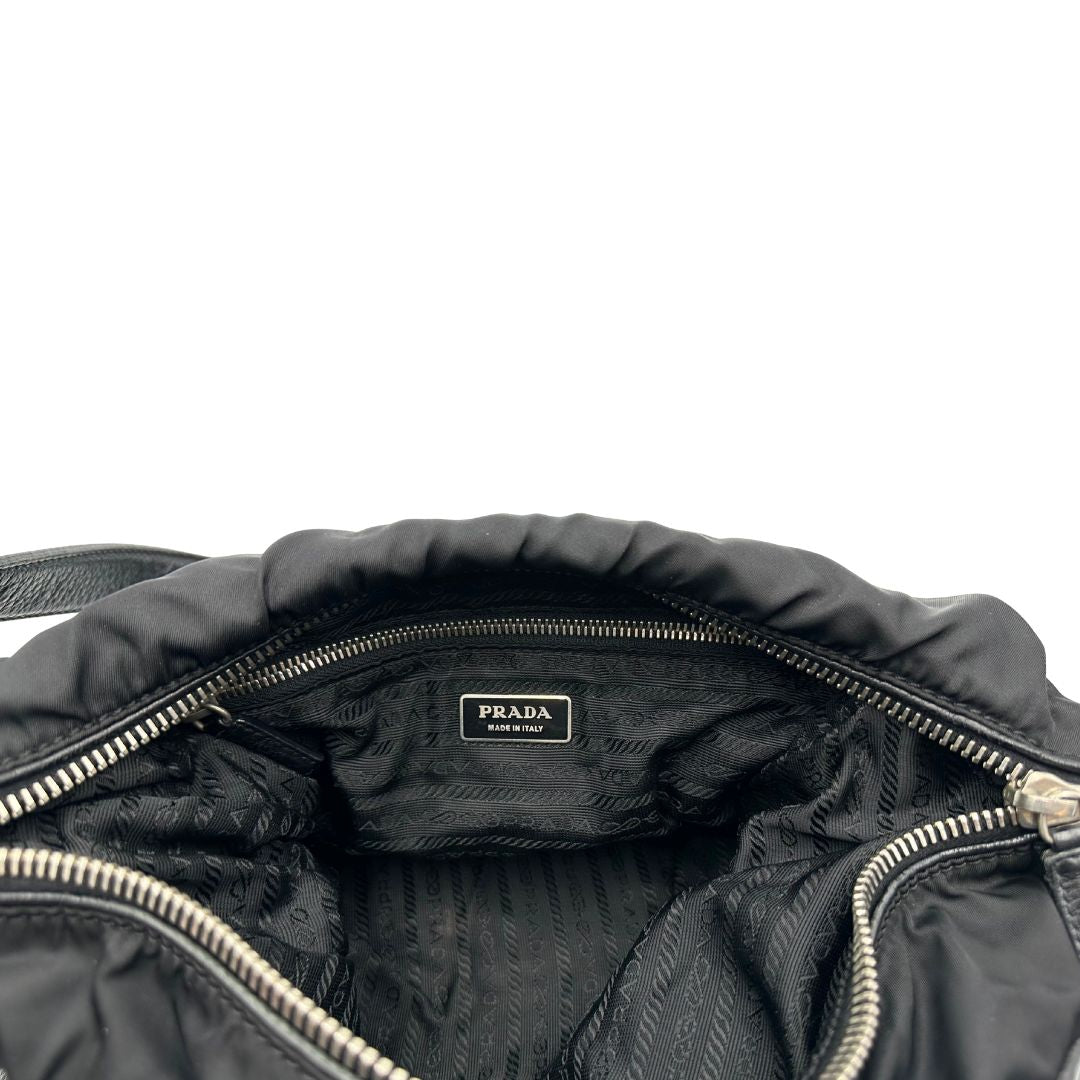 Tasca interna di una Borsa Prada in nylon nero con parti metalliche argentate e dettagli in pelle tono su tono. Munita di una tracolla regolabile con fibbie, rifinita con logo triangolare sul lato destro. Originale, usata, di lusso, in condizioni buone.